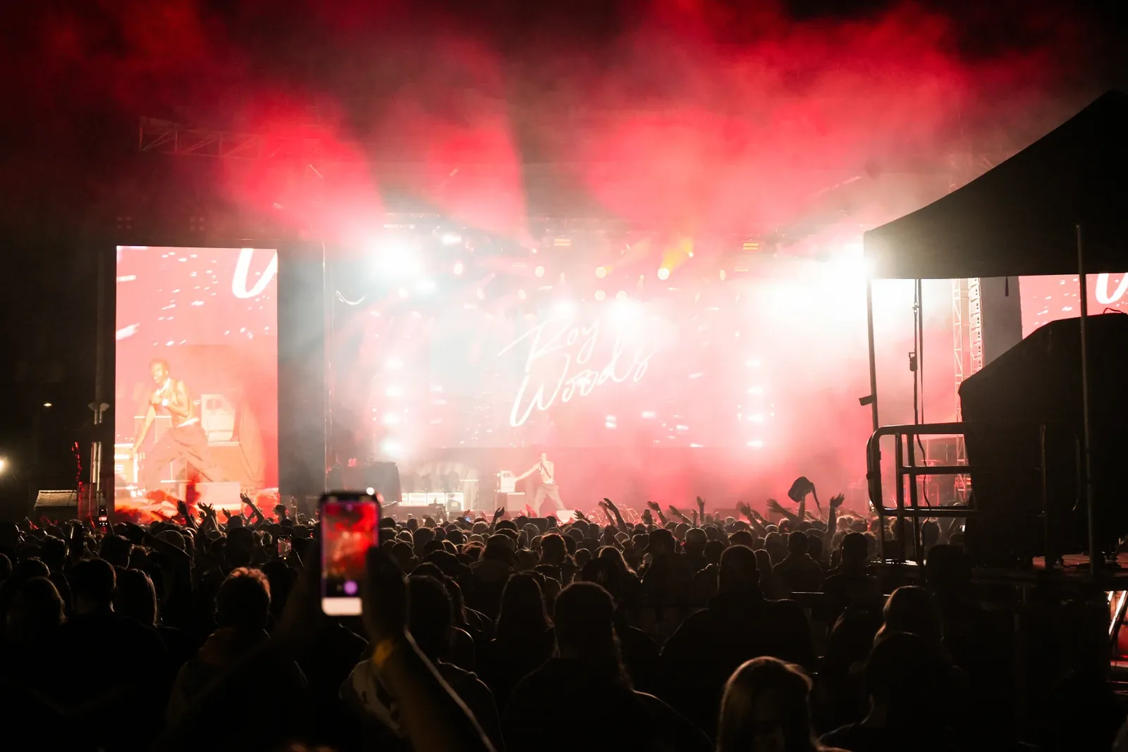A festival crowd facing a stage filled with red light and haze